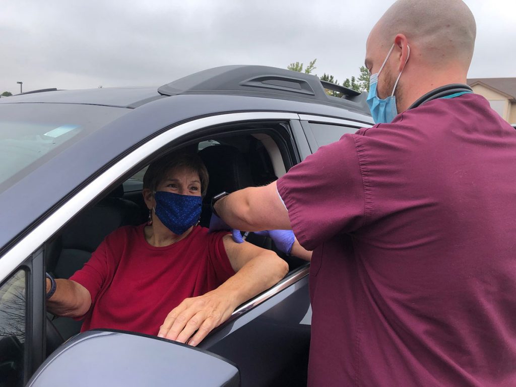 Woman gets her flu shot while sitting in her car, by way of a nurse. She is one of many getting flu shots curbside this year.