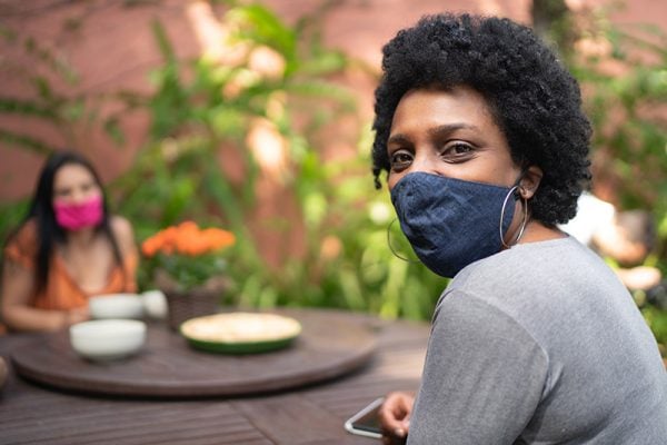 to prevent superspreader events, wear masks, avoid creeds, stay apart and gather outside. Some women wearing masks sit at an outdoor table.