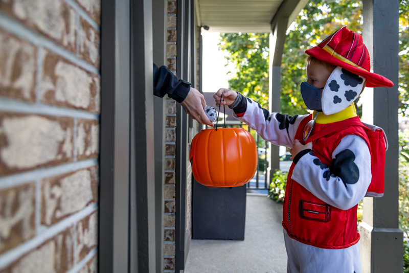 Child in paw patrol outfit gets a bag of candy from a hand out the door. UCHealth provides tips on how to do Halloween safely during covid.