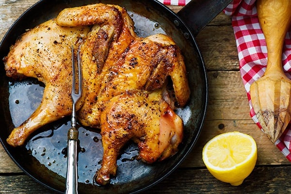 chicken under a brick shown in a cast iron skillet.