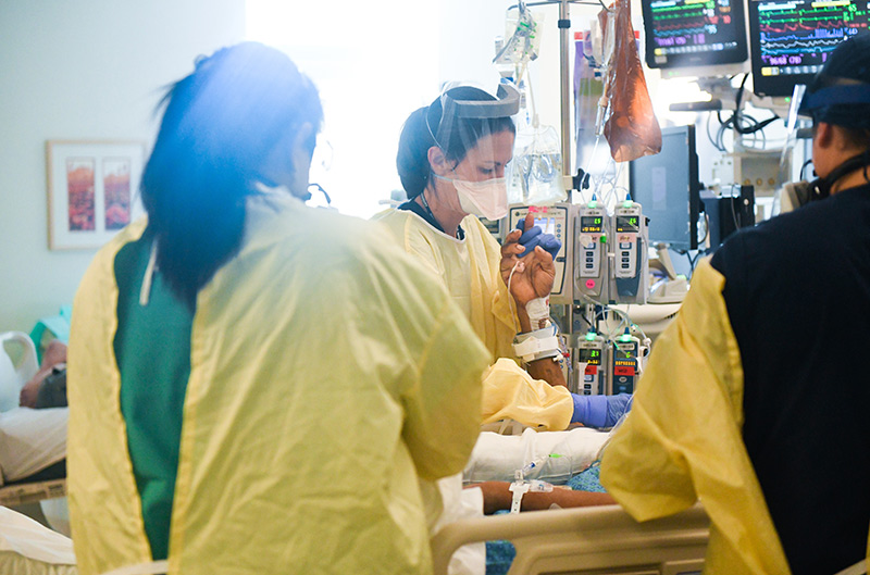 Pandemic nurse, Olivia Thorton, center, holds a patient's hand in a COVID-19 ICU at UCHealth University of Colorado Hospital.
