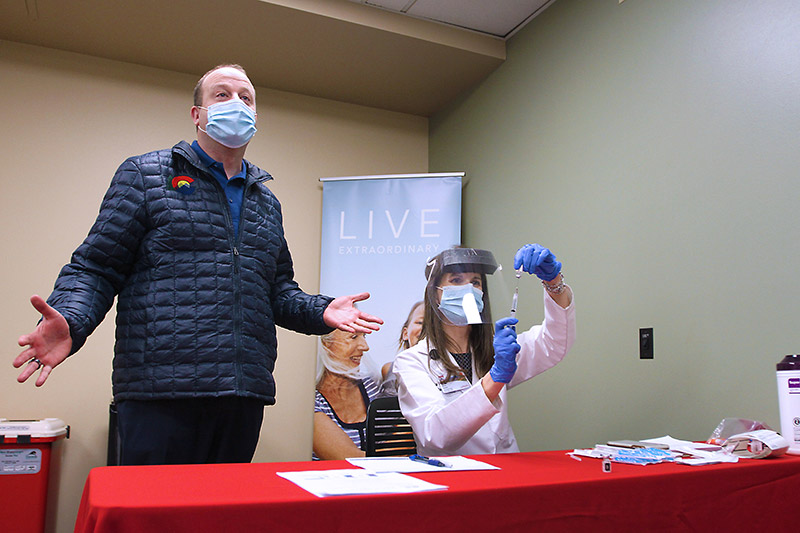 Colorado Gov. Jared Polis talks about Colorado's vaccine distribution plan as Gina Harper, a pharmacy services coordinator with UCHealth, prepares the first vial of Pfizer-BioNTech COVID-19 vaccine before it is administered to the first health care worker in the Colorado at UCHealth Poudre Valley Hospital in Fort Collins, Colo. on Monday, Dec. 14, 2020. Photo by Joel Blocker for UCHealth.