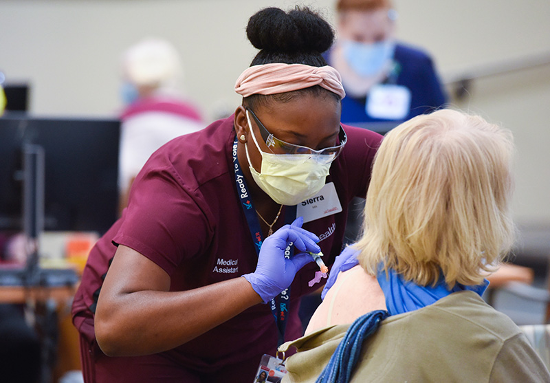 Nurse give a woman a vaccine. People should continue to wear their masks after their COVID-19 vaccine to keep others safe.