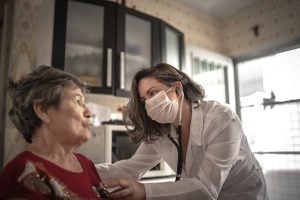 A doctor uses a stethoscope to hear any heart problems of an older woman who recovered from COVID..