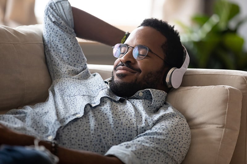 man listening to music while relaxing on the couch can be a great way to benefit from music.