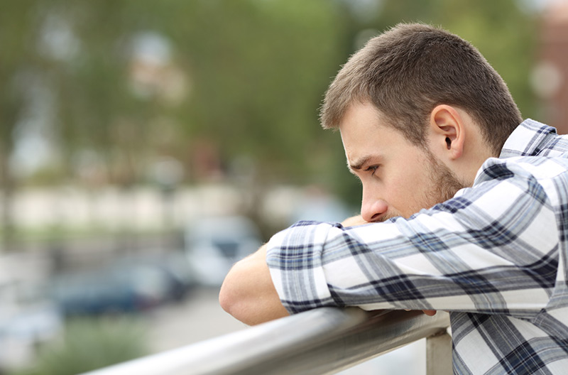 man with suicidal ideation looks sad as he looks over a balcony.