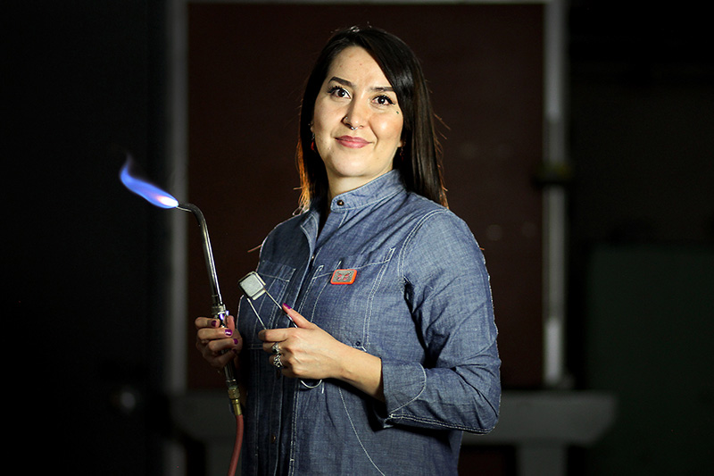 Priscilla Gonzalez holding a metalsmith torch. Her art demonstrates her efforts for colon cancer awareness.
