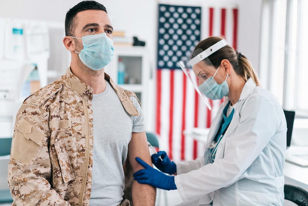 A man in a military uniform receives a vaccine. The military is looking for volunteers to help spot COVID-19 early.