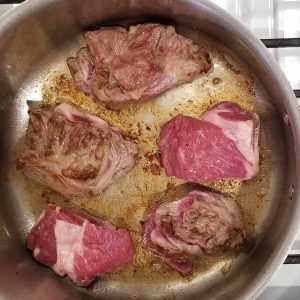 Photo of meat cooking in a pan.